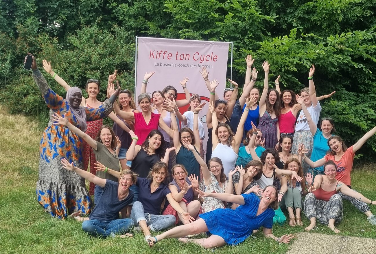 Une promotion de l'Académie Kiffe ton Cycle, bras levés, dans un jardin